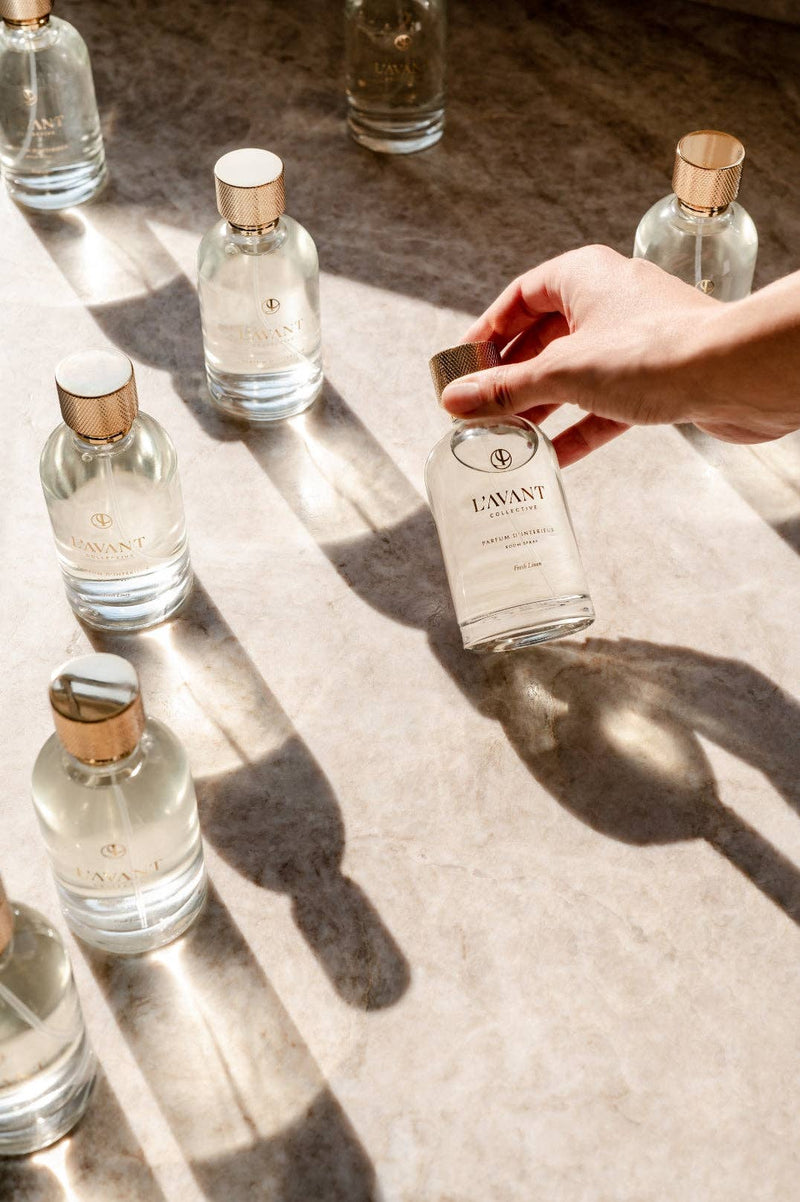 L'AVANT Collective Fresh Linen Room Spray 100 ml, held in a hand, showcasing its elegant design and luxurious scent appeal.