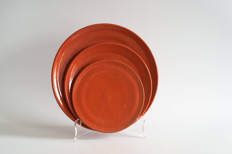RachaelPots - Dessert Plate: Sage, a set of three orange-glazed ceramic plates, displayed nested on a stand, ideal for serving desserts.