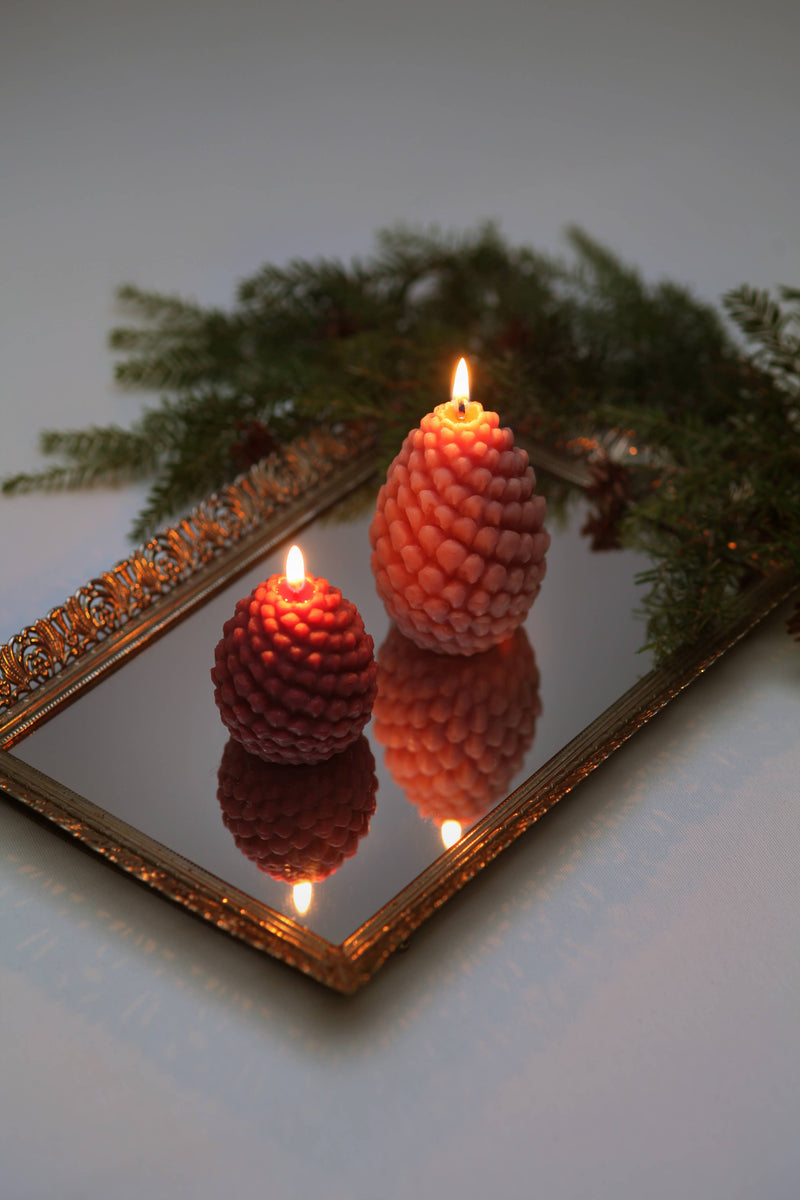 Mo&Co Home Exclusive: Sculpted Beeswax Pine Cones on a gold mirror tray, with evergreen sprig, reflecting warm, festive elegance.