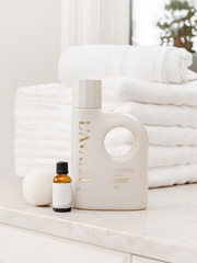 L'AVANT Collective - Fresh Linen Laundry Oil bottle beside towels, ideal for enhancing laundry with a natural, elegant scent blend.