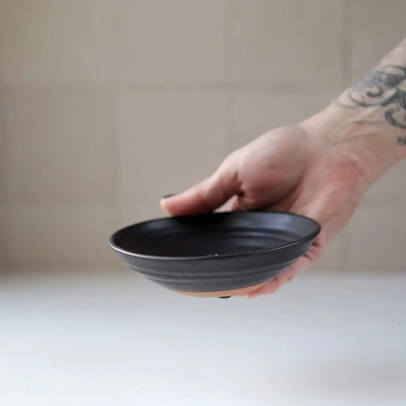 Hand holding Gravesco Pottery Incense Burner, a black ceramic dish for incense sticks, showcasing handcrafted design with visible unglazed clay edge. Ideal for catching ash.