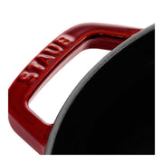 Staub | Round Cocottes - 7 qt Grenadine handle detail, showing red enameled cast-iron with STAUB embossed; glimpse of black interior.