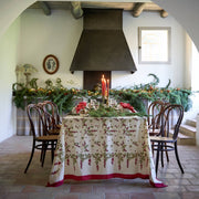 Couleur Nature - Gooseberry Red & Green French Tablecloth elegantly drapes a holiday table with evergreen garland, red candles, and festive settings in a rustic dining room.