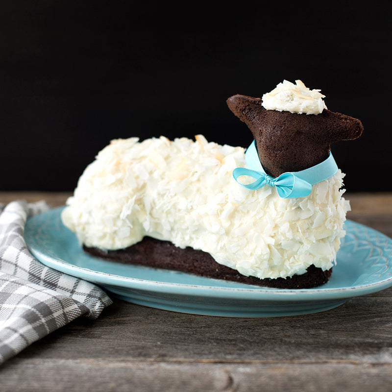 3D Lamb Cake Pan by Nordic Ware, shown with a decorated chocolate sheep cake featuring white frosting and a blue ribbon, ideal for Easter baking.