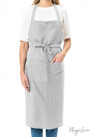 Woman wearing MagicLinen - Charcoal Grey Linen Bib Apron with Pockets, ideal for cooking or gardening, emphasizing practicality and style for kitchen tasks.