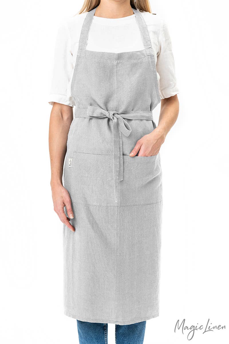 Woman wearing MagicLinen - Charcoal Grey Linen Bib Apron with Pockets, ideal for cooking or gardening, emphasizing practicality and style for kitchen tasks.