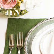 Crown Linen Designs | Hemstitch Placemat - Evergreen displayed with a silver fork on a dining table setting, highlighting the elegant hemstitch border pattern.