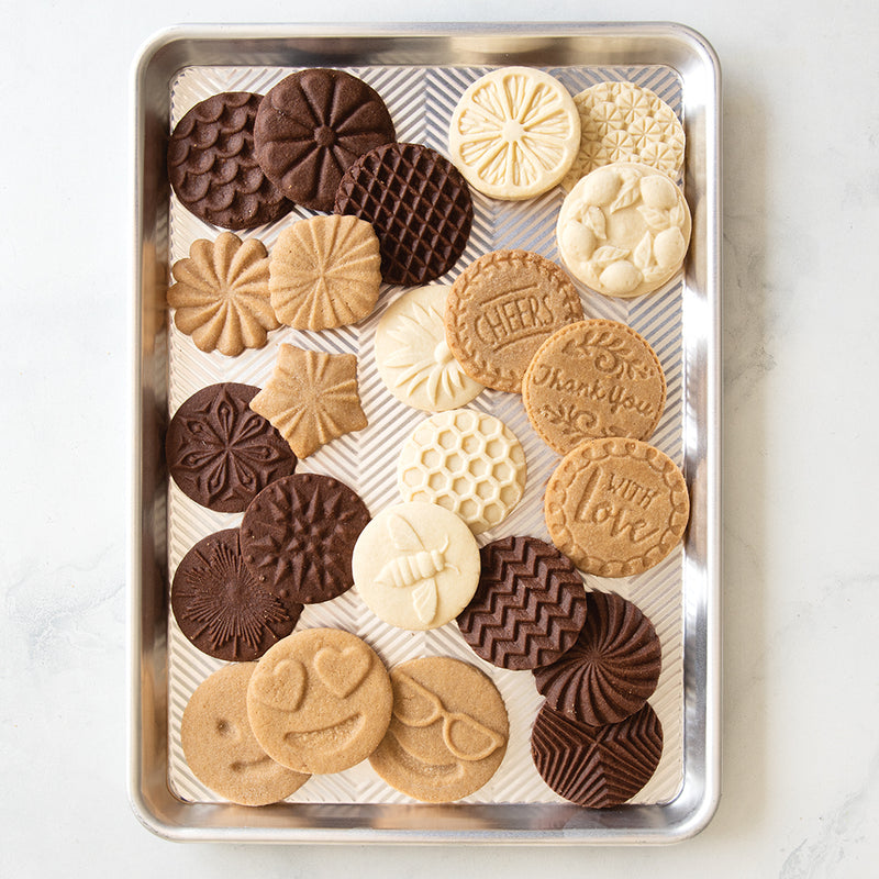 Nordic Ware | Honey Bees Cookie Stamps displayed on a tray of intricately designed cookies, showcasing bee, flower, and honeycomb patterns for delightful spring-themed baking.