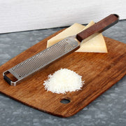 Microplane Master Series Zester with Walnut Handle on cutting board, shown grating cheese, highlighting its precision and versatility in food preparation.