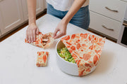 Hands in a kitchen using Bee's Wrap - Assorted 3 Pack - Mushroom Magic, Limited Edition, to wrap food, showcasing eco-friendly, reusable food storage.
