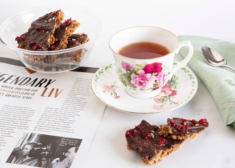 Norwegian Baked - KnekkeGodis sweet treat on a plate, featuring crispbread with caramel, dark chocolate, cranberries, and sea salt, accompanied by a floral teacup.