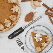 Microplane Premium Classic Spice Rasp Grater beside a pumpkin pie scene with grated cinnamon, showcasing its use for finely grating spices like nutmeg.