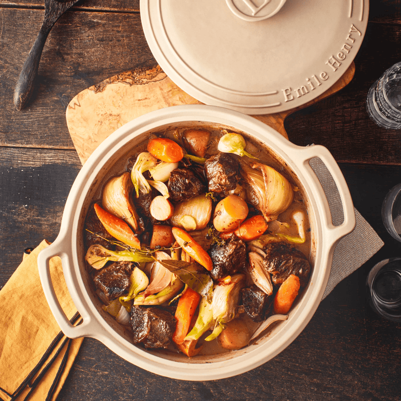 Emile Henry | Sublime 4 qt. Braiser, Graphite, filled with beef stew ingredients, showcasing its versatile cooking prowess on a rustic wooden table.