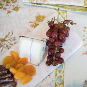 Couleur Nature - Pepe Marble Cheese Board, Large White, displaying goat cheese, grapes, dried apricots, and salami on a floral tablecloth, ideal for elegant gatherings.