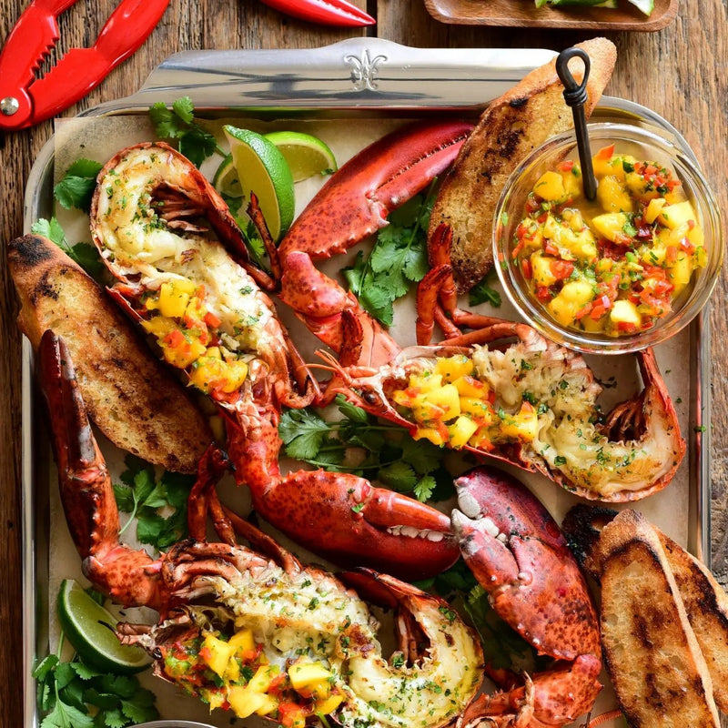 Seafood platter on Hestan | OvenBond Tri-Ply Bakeware, Single Half Sheet Pan, featuring grilled lobster halves with mango salsa, cilantro, lime, and bread slices.