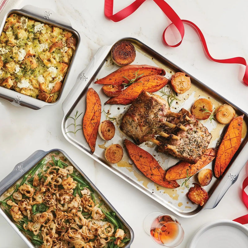Hestan Provisions | Oven Bond Tri-Ply 5 Piece Set in use with holiday dishes: stuffing, roasted lamb, green-bean casserole, and wine, perfect for festive cooking.