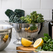 Hestan Provisions Stainless Steel Colander (5 Quart) on marble countertop, surrounded by fresh produce, showcasing its durability and efficiency for kitchen tasks.