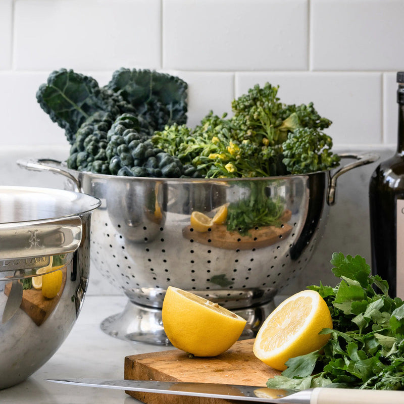 Hestan Provisions Stainless Steel Colander (5 Quart) on marble countertop, surrounded by fresh produce, showcasing its durability and efficiency for kitchen tasks.