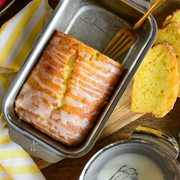 Hestan Provisions | OvenBond Tri-Ply Bakeware, 1-Pound Loaf Pan showcasing a glazed lemon loaf with a slice on a board, emphasizing craftsmanship and even baking.
