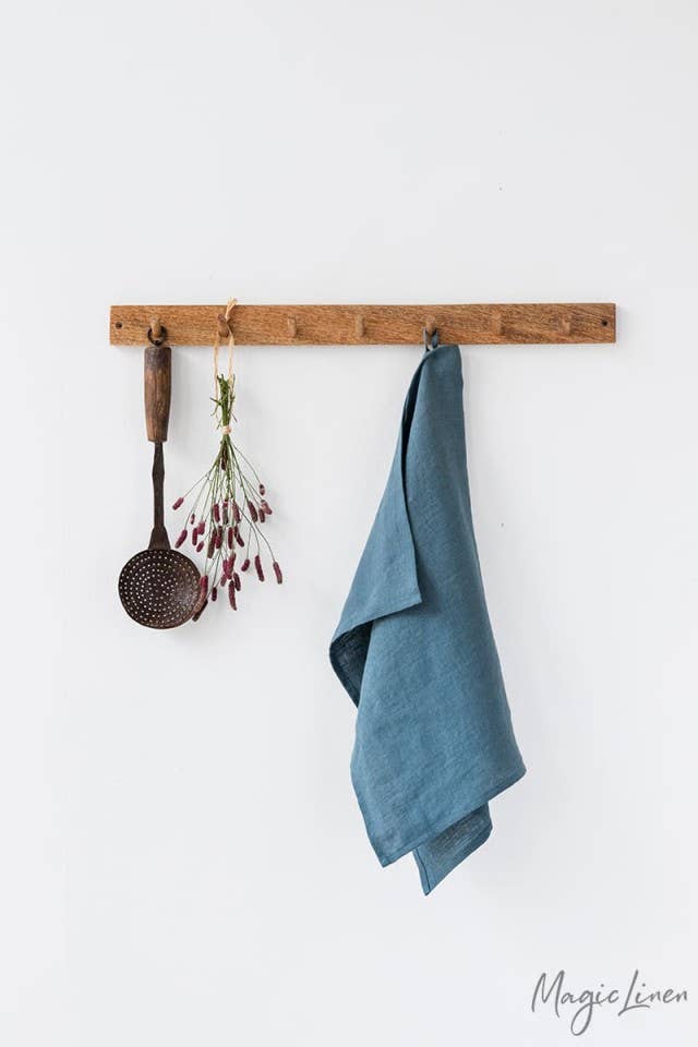 Wooden rack displaying a MagicLinen linen tea towel, hanging with kitchen utensils. Durable, absorbent, and ideal for maintaining a tidy kitchen.