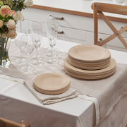 bambu® Disposable Bamboo Round Plates: 11 inches, neatly stacked on a linen-draped dining table, alongside glassware and a vase with roses, showcasing eco-friendly elegance.