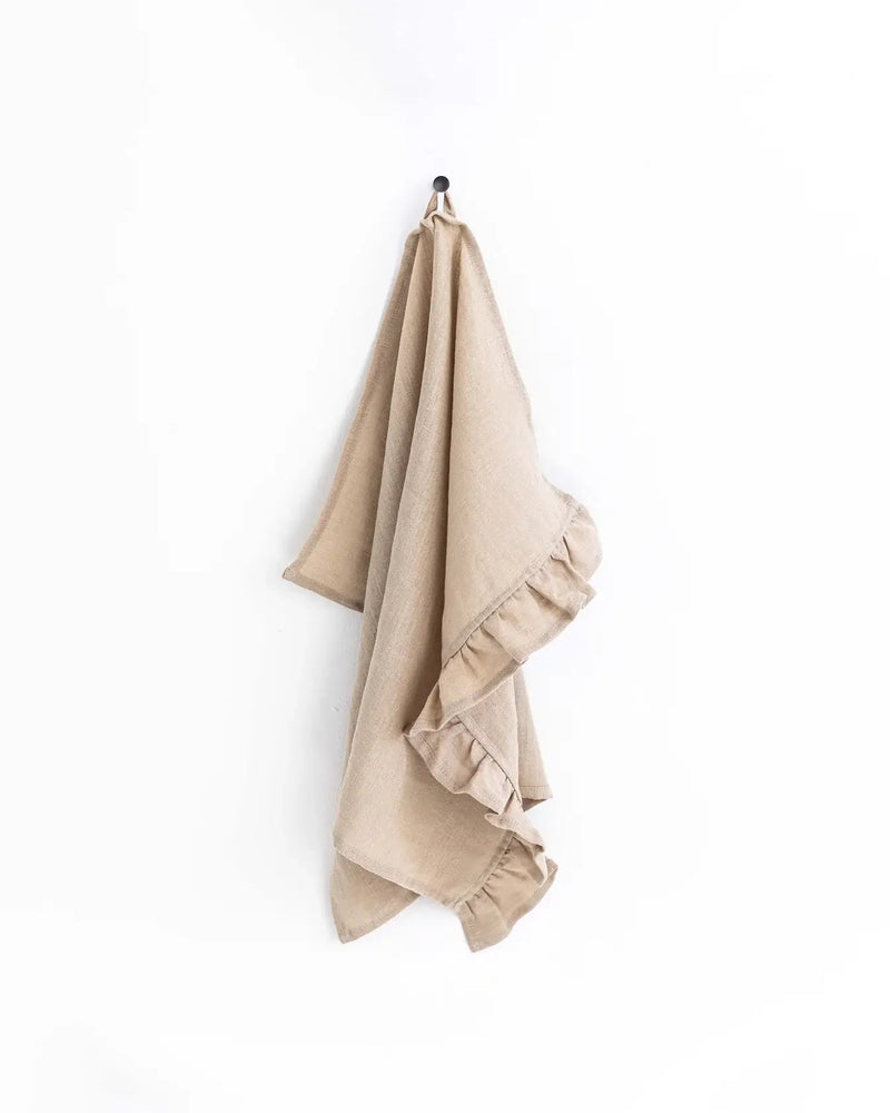 Ruffle trim linen tea towel hanging on a hook, showcasing its soft texture and practical loop for easy kitchen use.