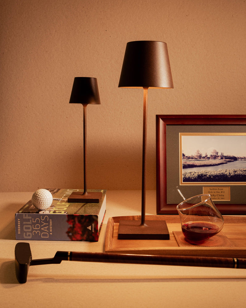 Zafferano America - Poldina Pro Cordless Lamp: Rust, featured with golf items, wine glass, and elegant accent lighting, highlighting its versatility and modern design.