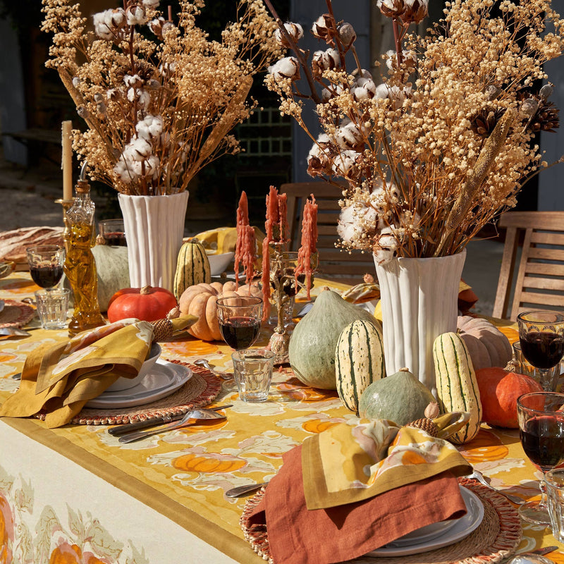 Caravan Home - Pumpkin Orange & Mustard Tablecloths adorn a cozy autumn tablescape with pumpkins, squash, and candles, perfect for fall gatherings.