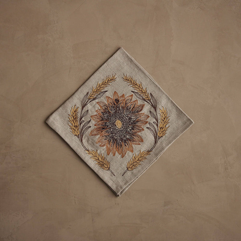Coral & Tusk - Sunflower and Wheat Dinner Napkin: Neutral-tone linen with embroidered sunflower and wheat wreath, perfect for autumn harvest table settings. Measures 20 × 20.