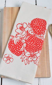 Hearth and Harrow's Strawberry Tea Towel, an organic cotton design featuring red strawberry prints, displayed with a wooden spoon for a charming kitchen accent.