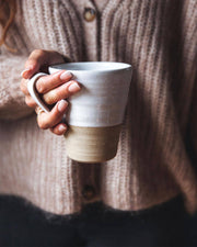 Farmhouse Pottery - Tall Silo Mug: Single, held by a hand in a chunky knit cardigan. Features a natural clay base and white glaze, ideal for stylish, large sips.