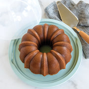 Nordic Ware | Translucent Bundt® Cake Keeper on a plate with a cake server, designed for secure cake storage and transportation, ideal for keeping cakes fresh.