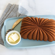 Nordic Ware Loaf Cake Keeper with a loaf of bread and butter on an elegant scalloped tray, ideal for storing and serving baked goods.