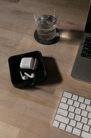 Graf Lantz - Kobon Leather Square Tray - Black, elegantly holds white earbuds and office essentials on a desk, showcasing versatility and sophistication.