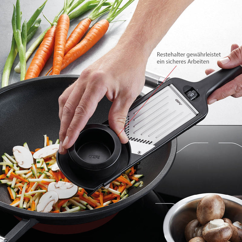 A person uses the GEFU | Violi 2.0 Adjustable Mandoline to grate vegetables into a pan, highlighting its functionality for kitchen tasks.