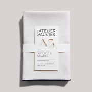 ATELIER SAUCIER - Cream Burlap Noir Napkins | Set of 4, featuring soft burlap linen with black edging, neatly wrapped in a branded paper band.