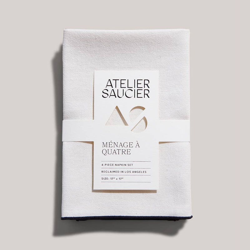 ATELIER SAUCIER - Cream Burlap Noir Napkins | Set of 4, featuring soft burlap linen with black edging, neatly wrapped in a branded paper band.