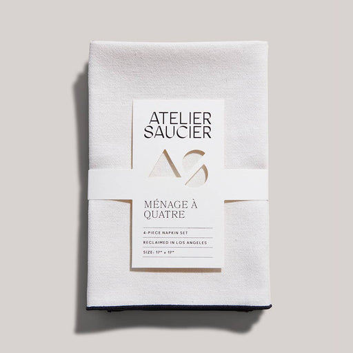 ATELIER SAUCIER - Cream Burlap Noir Napkins | Set of 4, featuring soft burlap linen with black edging, neatly wrapped in a branded paper band.