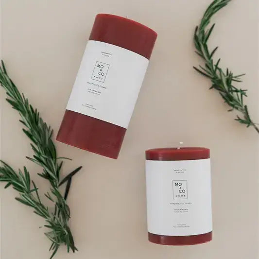 Mo&Co Home - 100% Beeswax Pillar Candles: Two deep-red hand-poured candles with rosemary sprigs, showcasing eco-friendly design, perfect for home decor and special occasions.