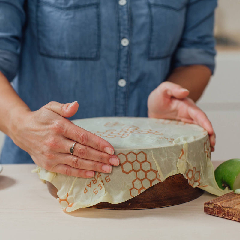 Bee's Wrap - Large 3 Pack Wraps shown covering a round wooden bowl, highlighting its reusable, sustainable design for preserving food in the kitchen.