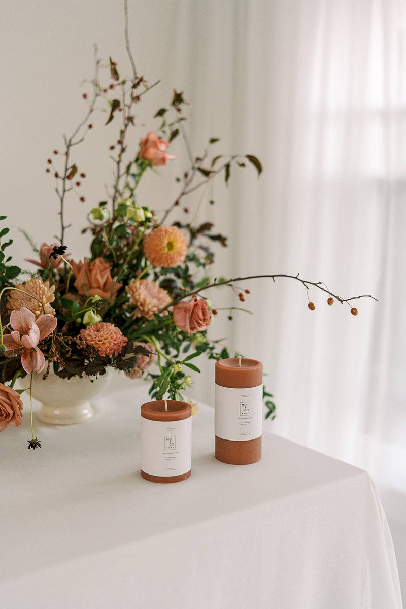 Mo&Co Home - 100% Beeswax Pillar Candles | Terra Cotta: 3x6 Inch displayed alongside flowers, showcasing an eco-friendly, clean-burning candle ideal for home decor and celebrations.
