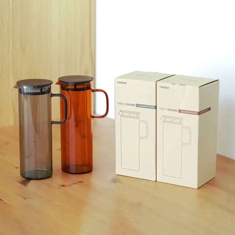 HARIO USA - HARIO Colors Glass Cold Brew Pitcher, 800ml: Amber, with built-in metal filter, showcased alongside its box on a wooden table.