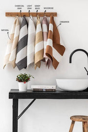 Striped linen tea towel with a hanging loop, showcased in a bathroom setting with towels and plants, emphasizing zero-waste design and practical kitchen use.
