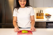 Bee's Wrap - Assorted 3 Pack - Splendid Spring: A woman cuts a pear wrapped in eco-friendly, reusable fabric food storage wrap.