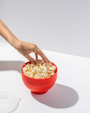 Hand reaching for popcorn in W&P's Standard Size Popcorn Popper, a silicone, reusable maker ideal for microwave popcorn, available at Athens Cooks.