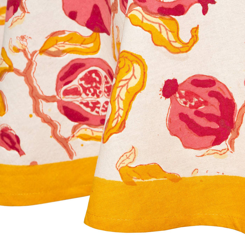 Close-up of Couleur Nature - Pomegranate Yellow & Red 71 x 71 French tablecloth with stylized red pomegranates and mustard-yellow hem, highlighting vibrant Southern France-inspired design.