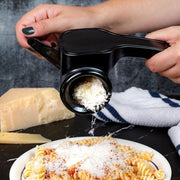 Person using a Microplane Rotary Grater to grate cheese over a plate of pasta.