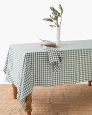 Linen tablecloth in Forest green gingham, 59x59 inches, displayed on a wooden dining table with a vase of flowers, enhancing cozy dining experiences.
