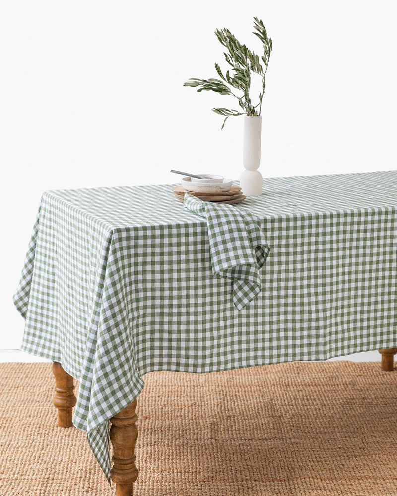 Linen tablecloth in Forest green gingham, 59x59 inches, displayed on a wooden dining table with a vase of flowers, enhancing cozy dining experiences.