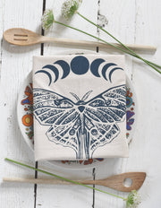 Hearth and Harrow - Organic Cotton Luna Moth Tea Towel displayed on a floral plate, accompanied by wooden spoons and wildflowers, showcasing eco-friendly kitchen elegance.